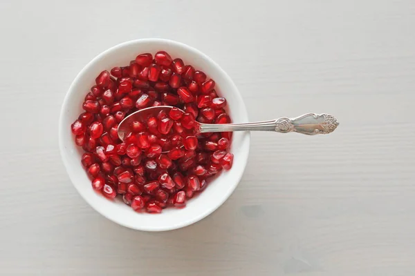 Körner roter reifer Granatäpfel liegen in einer weißen Schüssel mit einem Löffel. — Stockfoto