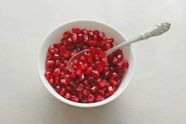 Korrels van rode rijpe granaatappel liggen in een witte kom met een lepel. — Stockfoto