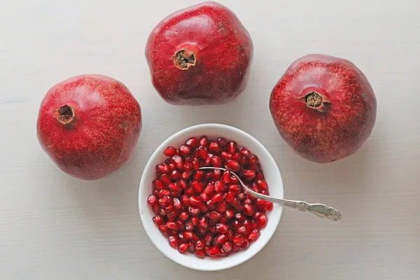 Korrels van rode rijpe granaatappel liggen in een witte kom met een lepel. — Stockfoto