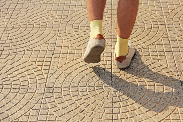 Men's Feet in Light Shoes and Yellow Socks Go along the Road. Th