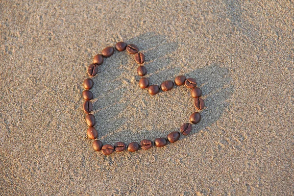 Heart of coffee. Grains of coffee are laid out on sand in the fo