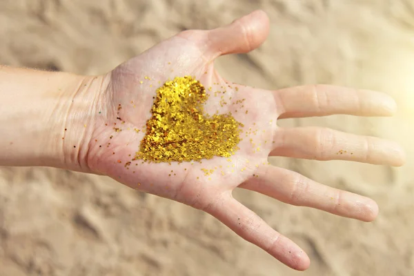 Un corazón resplandeciente dorado yace en las manos de la niña. Corazón en t —  Fotos de Stock