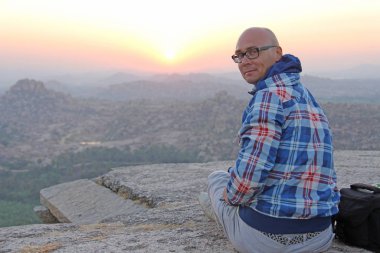 Gözlük yakışıklı kel bir adam bir günbatımı veya şafak backgrou oturur