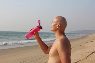 Çıplak ya da çıplak gövdeli kel, yakışıklı bir adam su içiyor.