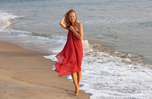 Ένα όμορφο κορίτσι με ξανθά μαλλιά, με ένα κόκκινο φόρεμα, περπατά κατά μήκος του — Φωτογραφία Αρχείου