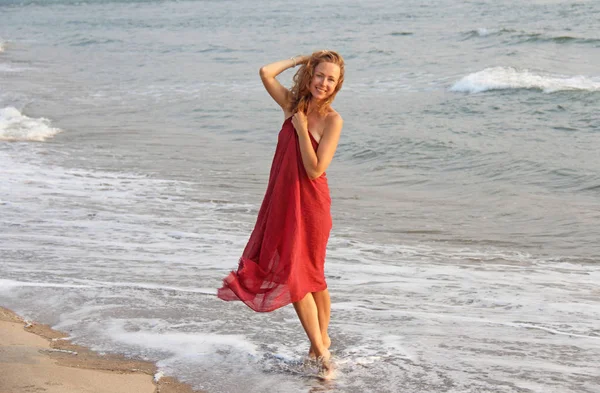 Ένα όμορφο κορίτσι με ξανθά μαλλιά, με ένα κόκκινο φόρεμα, περπατά κατά μήκος του — Φωτογραφία Αρχείου