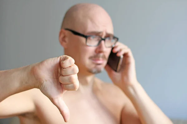 Young handsome bald man in black glasses talking on the phone. C