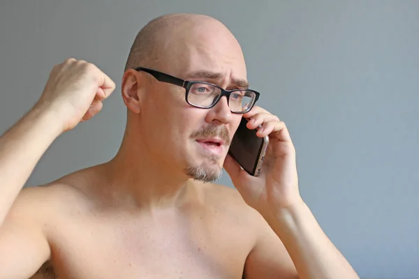 Young handsome bald man in black glasses talking on the phone. C