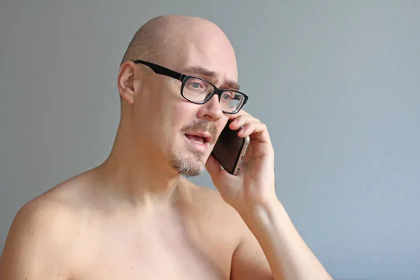 Young handsome bald man in black glasses talking on the phone. C
