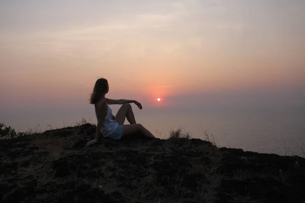 바다와 태양을 배경으로 산에 앉아 있는 소녀 — 스톡 사진