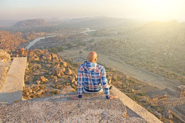 A handsome bald man in glasses sits with his back on a sunset or