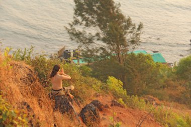Bir adam bir dağın tepesinde oturur ve mesafe içine bakar, üzerinde 