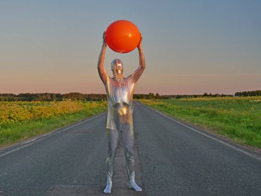 Gümüş takım elbiseli uzun boylu, zayıf bir adam. Dar gümüş takım elbiseli. Yazın boş bir yolda duruyor. Kaçık, uzaylı, olağanüstü bir insan, UFO..