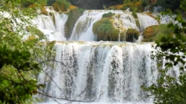 Şelaleler Krka, Ulusal Park, Hırvatistan. Ağaçlar ve çimenler arasındaki Krka Milli Parkı 'nda şelale çağlayanı gibi güzel nehirler yavaşça akar. Suyun, nehrin, akıntının, şelalenin yavaş çekim videosu.