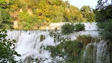 Şelaleler Krka, Ulusal Park, Hırvatistan. Ağaçlar ve çimenler arasındaki Krka Milli Parkı 'nda şelale çağlayanı gibi güzel nehirler yavaşça akar. Suyun, nehrin, akıntının, şelalenin yavaş çekim videosu.