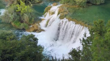 Şelaleler Krka, Ulusal Park, Hırvatistan. Ağaçlar ve çimenler arasındaki Krka Milli Parkı 'nda şelale çağlayanı gibi güzel nehirler yavaşça akar. Suyun, nehrin, akıntının, şelalenin yavaş çekim videosu.