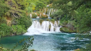 Şelaleler Krka, Ulusal Park, Hırvatistan. Ağaçlar ve çimenler arasındaki Krka Milli Parkı 'nda şelale çağlayanı gibi güzel nehirler yavaşça akar. Suyun, nehrin, akıntının, şelalenin yavaş çekim videosu.