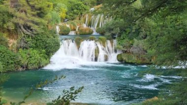 Şelaleler Krka, Ulusal Park, Hırvatistan. Ağaçlar ve çimenler arasındaki Krka Milli Parkı 'nda şelale çağlayanı gibi güzel nehirler yavaşça akar. Suyun, nehrin, akıntının, şelalenin yavaş çekim videosu.