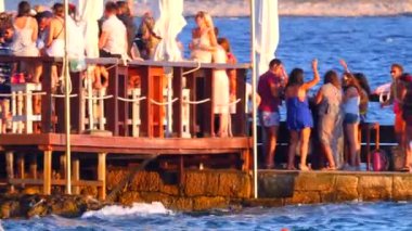 Hırvatistan, Hvar Adası, 15 Ağustos 2019. Birçok genç insan deniz kıyısında müzik eşliğinde dans edip kokteyl içer. Gün batımında mayo giymiş bir yaz partisi. Eğlence ve gençlik eğlencesi.