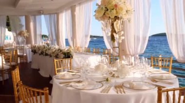 Hırvatistan 'ın Hvar adasındaki deniz kıyısında, beyaz-altın renkli düğün masasının güzel dekorasyonu. Denizde düğün. Altın çatal bıçak takımı. Güzel bir düğün. Zarif altın ve beyaz masa..