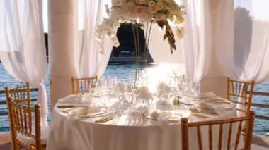 Hırvatistan 'ın Hvar adasındaki deniz kıyısında, beyaz-altın renkli düğün masasının güzel dekorasyonu. Denizde düğün. Altın çatal bıçak takımı. Güzel bir düğün. Zarif altın ve beyaz masa..