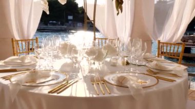 Hırvatistan 'ın Hvar adasındaki deniz kıyısında, beyaz-altın renkli düğün masasının güzel dekorasyonu. Denizde düğün. Altın çatal bıçak takımı. Güzel bir düğün. Zarif altın ve beyaz masa..