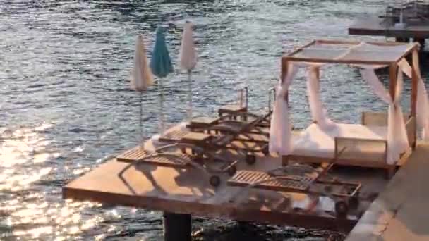 Empty wooden deckchairs, beautiful tents for sunbathing, relaxing tents on seashore, bay in Croatia, island of Hvar. Evening sea sunset, relaxation, vacation. Lounge chairs, ready to take rest people. — Stock Footage Empty Wooden Deckchairs Beautiful Tents Sunbathing Relaxing Tents Seashore Bay Royalty Free Stock Footage