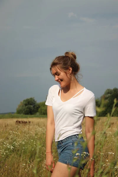 白いTシャツを着た金髪の魅力的な美しい女性の肖像画と小麦畑のジーンズのショートパンツ — ストック写真