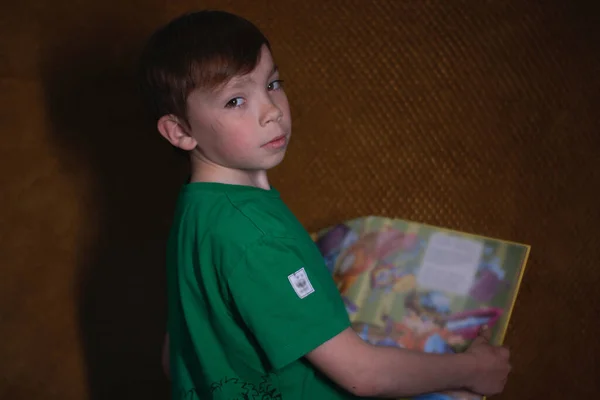 Retrato de un niño rubio de nueve años con una camiseta verde sobre fondo marrón leyendo un libro amarillo —  Fotos de Stock