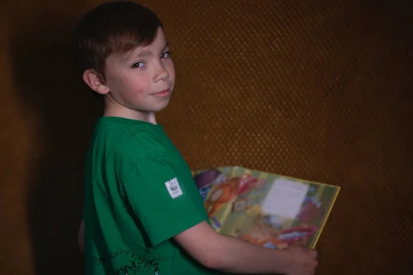 Retrato de un niño rubio de nueve años con una camiseta verde sobre fondo marrón leyendo un libro amarillo —  Fotos de Stock