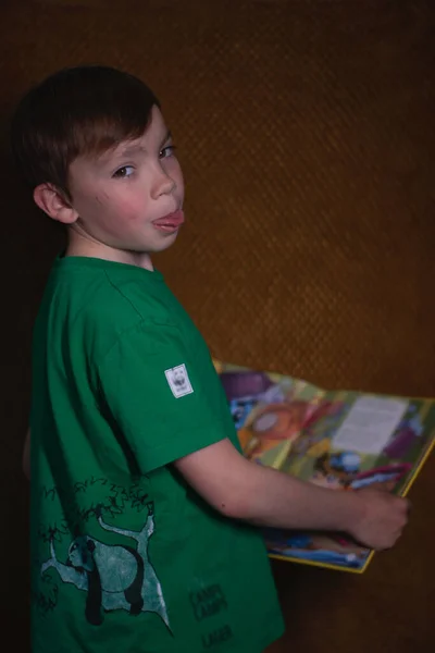 Retrato de un niño rubio de nueve años con una camiseta verde sobre fondo marrón leyendo un libro amarillo —  Fotos de Stock