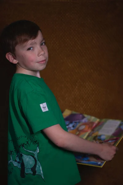 Retrato de un niño rubio de nueve años con una camiseta verde sobre fondo marrón leyendo un libro amarillo —  Fotos de Stock