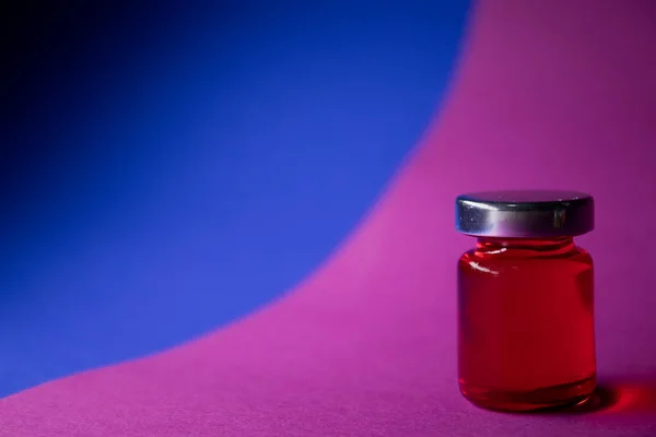 Kis üveg piros folyadékkal, kék-rózsaszín háttérrel. Elszigetelve. Társasjátékok. Gyógymód - gyógyszer, vakcina. Coronavirus vagy covid-19 - pandémia — Stock Fotó