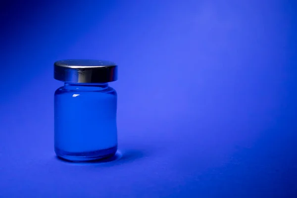 Kis üveg kék folyadékkal, kék háttérrel. Elszigetelve. Társasjátékok. Gyógymód - gyógyszer, vakcina. Coronavirus vagy covid-19 - pandémia — Stock Fotó