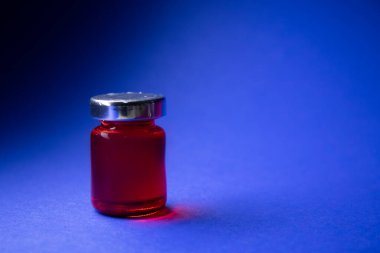 Mavi arka planda kırmızı sıvı olan küçük bir şişe. İzole edilmiş. Masa oyunları. Tedavi, ilaç, aşı. Coronavirus veya covid-19 - salgın