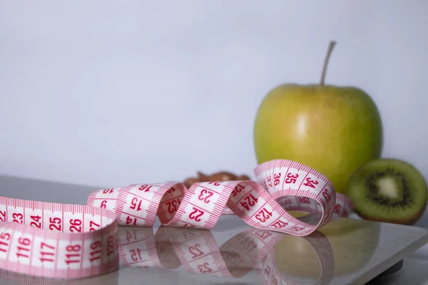 Cinta métrica roja, manzana, kiwi y almendras en escamas de baño beige. Dieta y Vida sana, pérdida de peso, concepto deportivo. Copiar espacio. Aislado. Fondo blanco — Foto de Stock