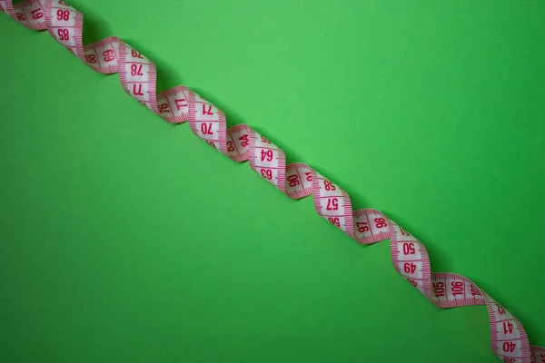 Red measuring tape on green background. Loss weight concept. Top view. Copy space. Isolated