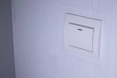 Plastik mekanik beyaz ışık anahtarı, açık gri bir duvara monte edilmiş.