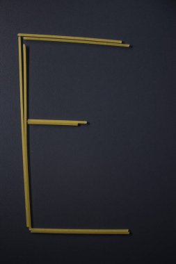 E harfi gri arka planda spagetti ile yazıldı, üst manzara, kopyalama alanı. Yiyecek malzemeleri, yiyecek bağışı. 