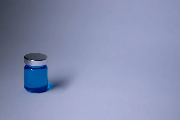 Pequena garrafa com líquido azul sobre fundo branco-cinza. Isolado. Cura - vacina. Coronavírus ou covid-19 - pandemia — Fotografia de Stock