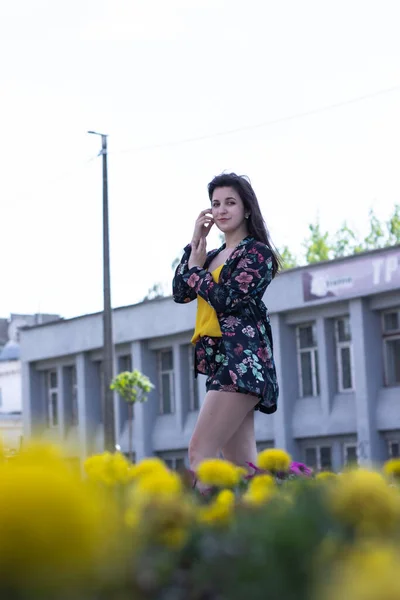 Atractiva mujer morena joven en camiseta amarilla y traje de pantalones cortos floridos. cerca de un arbusto de flores. espacio de copia . — Foto de Stock