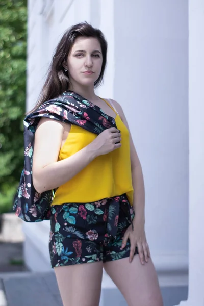 Atractiva mujer morena joven en camiseta amarilla y traje de pantalones cortos floridos. espacio de copia . —  Fotos de Stock