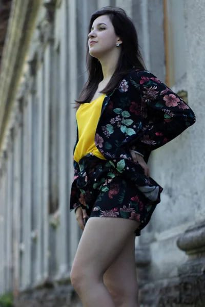 Mulher morena jovem atraente em camiseta amarela e traje de shorts floridos. Antecedentes antigos. espaço de cópia . — Fotografia de Stock