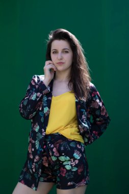Sarı tişörtlü ve çiçekli şort kostümlü çekici esmer kadın. Yeşil duvar arkaplanı. Boşluğu kopyala.