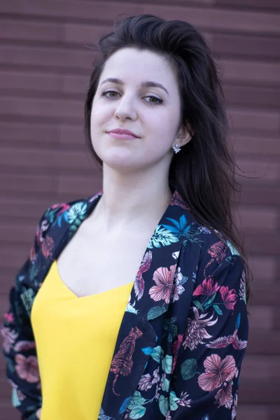 Vonzó fiatal barna nő sárga pólóban és virágos rövidnadrág jelmezben. barna fal háttér. másolás helye. — Stock Fotó