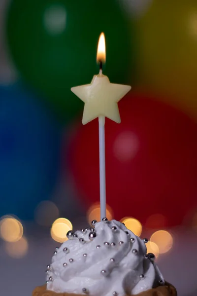 Festive cupcake with a yellow star-shaped candle. On the background - multi-colored balloons and lights. party, birthday concept. Copy space. — Stock Photo, Image