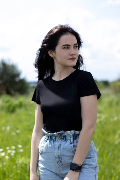 Encantadora joven morena con una camiseta negra y pantalones cortos de mezclilla. En el campo, en el jardín . —  Fotos de Stock