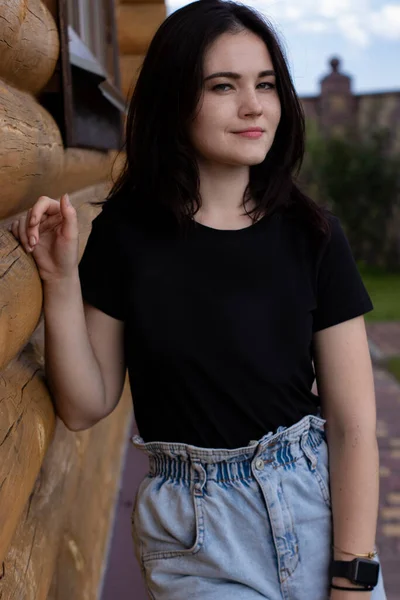 Привлекательная молодая брюнетка в черной футболке и джинсовых шортах рядом с деревянным современным домом — стоковое фото