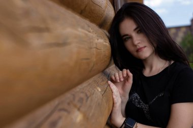 Ahşap modern bir evin yanında siyah tişörtlü ve kot şortlu çekici esmer kadın.