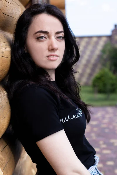 Atraente jovem morena mulher em t-shirt preta e calções jeans ao lado de uma casa moderna de madeira — Fotografia de Stock
